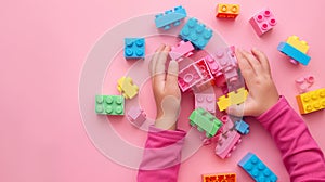 A child\'s hand playing with Lego. There are Legos scattered on the table with a pink background