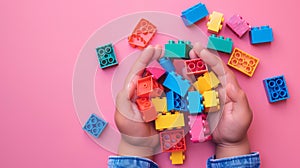 A child\'s hand playing with Lego. There are Legos scattered on the table with a pink background