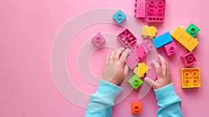 A child\'s hand playing with Lego. There are Legos scattered on the table with a pink background