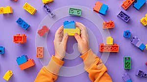 A child\'s hand playing with Lego. There are Legos scattered on the table with a purple background