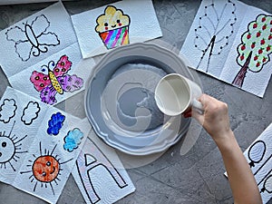 A child`s hand pours water from a Cup into a plate, for a child`s creative experience.