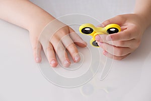 Child`s hand spinning a fidget spinner device. Top view. Playing with a yellow hand spinner fidget toy