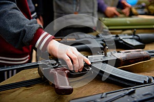 A child& x27;s hand takes an automatic rifle from the table with weapons. Close-up photo.