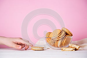 The child`s hand takes a cookie from a glass bowl on a pink background. The concept of breakfast and a quick snack
