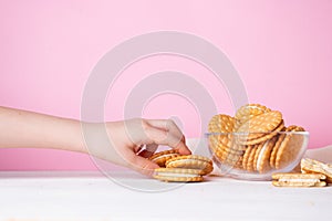 The child`s hand takes a cookie from a glass bowl on a pink background. The concept of breakfast and a quick snack