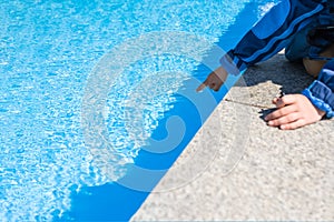 A child`s hand touches the blue water in the pool