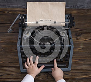 Child`s hand writing letter to Santa Claus on vintage typewriter in anticipation of the holiday of Christmas
