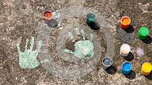 Child`s handprints on the concrete and colorful paint containers. Creativity, arts and crafts, children sensory integration art