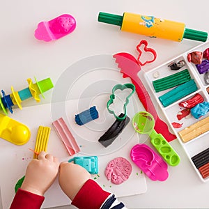 Child`s hands with colorful clay. Toddler playing and creating toys from play dough. Boy molding modeling clay