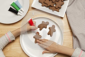 Child& x27;s hands decorating a christmas gingerbread cookies using colored glazeon, wooden table, top view. Christmas cookies