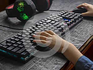 The child`s hands in a denim shirt playing the keyboards with gaming headphones.