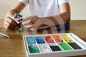 The child`s hands are engaged in modeling from plasticine on a table on which there is a box of plasticine, close-up, side view