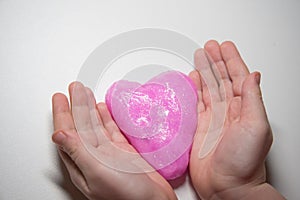 The child`s hands hold a slime in the form of a pink heart. Concept. Valentine`s day