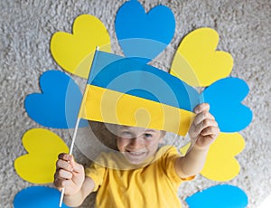 The child\'s hands hold the Ukrainian flag. the child lies among blue and yellow hearts