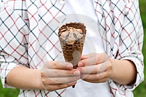 Child's hands holding chocolate brown ice cream in a waffle cone outdoors in summer