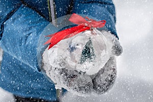 Child`s hands holding a christmas ball with a red ribbon outside