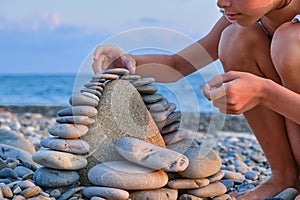 The child& x27;s hands lay pebbles, stones in a tower on the beach in summer, close-up.