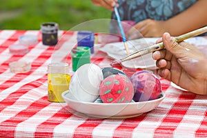 Child`s hands painting Easter eggs on a checkered tablecloth