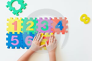 Child`s hands playing with numbers, learning simple multiplication. Colorful bright puzzle numbers on white background, education