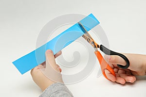 Child`s hands scissor a strip of blue paper on white background