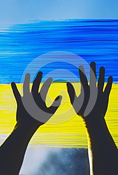 Child`s hands touch painting yellow-blue flag of Ukraine on window. Hands of little kid on image of flag of Ukraine on glass.