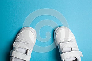 Child`s new white sport shoes or sneakers on the light blue pastel background.