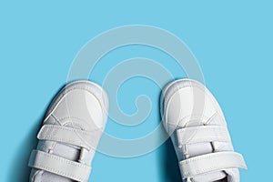 Child`s new white sport shoes or sneakers on the light blue pastel background