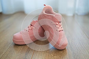 Child's pink sneakers on wooden floor. Cute girl's shoes on floor