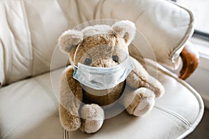 A child`s teddy bear sitting on a chair wearing a face mask