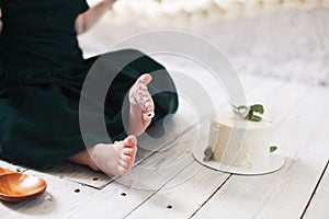 Child`s toes in the cake cream on the background of white wooden floor and white cake