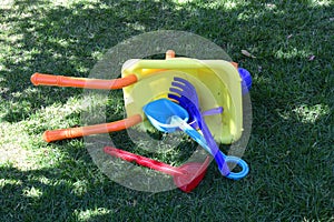 Child`s toy played on the grass in the park plastic children`s wheelbarrow with stuffed pa and fork
