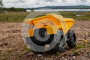 A child`s yellow dump truck abandoned on the ground by a lake