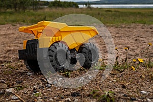 A child`s yellow dump truck abandoned on the ground by a lake, side on view