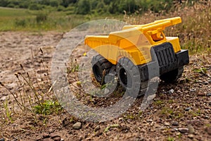 A child`s yellow dump truck abandoned on the ground by a lake, three quarter view
