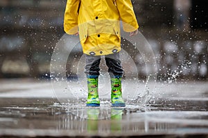 The child`s yellow raincoat and green boots fall into a puddle of water. Autumn rainy weather. A walk in the rain.