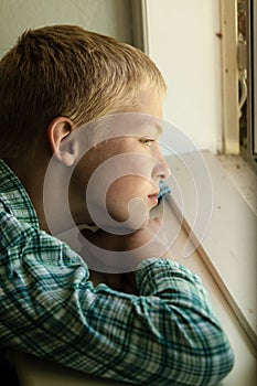 Child with sad expression sitting near window