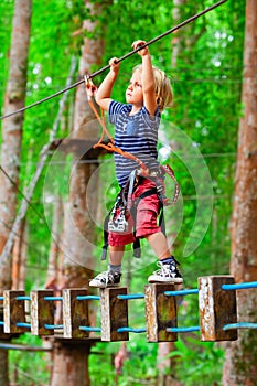 Child in safety harness pass obstacle in adventure rope park