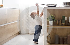 Child safety at home concept - toddler reaching for pan on the stove in kitchen