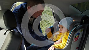 child safety, man puts male child in babyseat in back seat and buckle seat belts for traveling in car, give me five