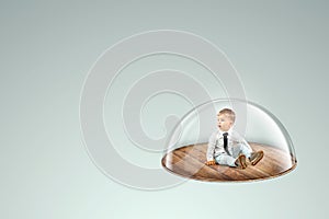 Child safety, overprotection, a little boy sits under a glass dome, cap. Vaccinations, protection against viruses and diseases,