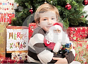 Child with santa doll in front of christmas tree