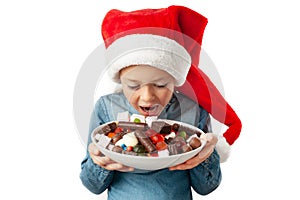 A child in a Santa hat adores sweets. A plate full of assorted chocolates in the hands of a little girl photo