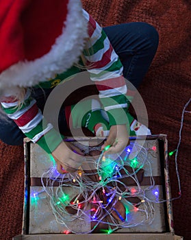 Child in a Santa hat and an elf sweater sits on a blanket, opens a gift box