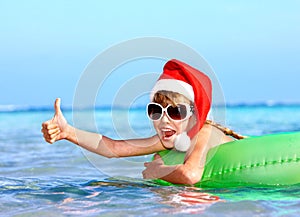 Child in santa hat floating on inflatable ring in sea.