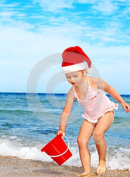 Child in santa hat playing on beach.