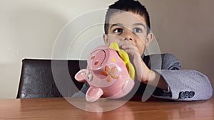Child savings. Preschool boy in a business suit turning and oppening a piggy banks. Finances for kids