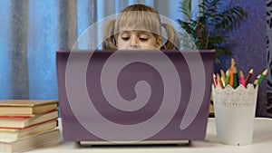 Child schoolgirl learning lessons, distance education at home sitting at table using laptop computer