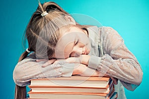 Child schoolgirl read Schoolgirl fell sleep on a stack of books. ing a book on blue background