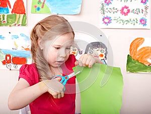 Child with scissors cut paper at home.