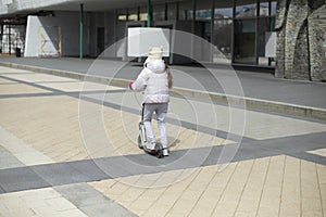 Child on scooter. Girl rides around square. Child travels by mechanical transport